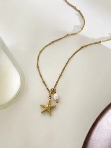 Close-up of golden starfish pendant necklace featuring a single freshwater pearl accent