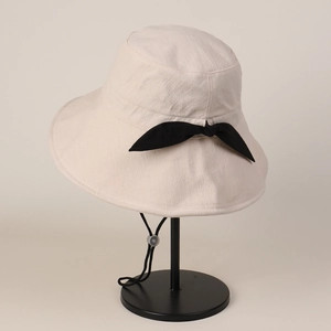 Detail of beige cotton linen sun hat featuring a black bow and adjustable chin strap