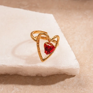 Dettaglio dell'anello a cuore dorato con gemma rossa e texture in metallo martellato