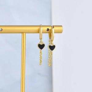 Golden heart drop earrings with black oil drip charms and long chains on display stand