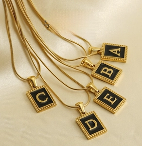 Detail of 18K gold-plated snake chains with black rectangular shell letter pendants