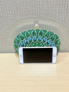 Green peacock clutch bag shown next to a smartphone for size reference and scale