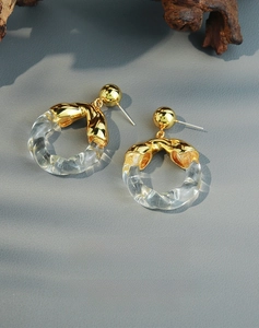 Detail of twisted gold metal earring with transparent resin ring on a textured surface