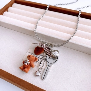 Detail of flocked bear and lucky key pendant on a silver steel chain over a jewelry tray