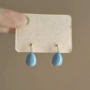 Detailed close-up of blue teardrop enamel earrings with elegant gold hooks on display card