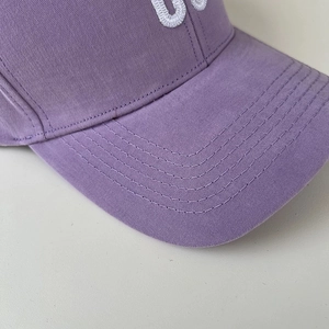 Detailed close-up of purple cotton baseball cap with white 3D embroidery and stitched brim