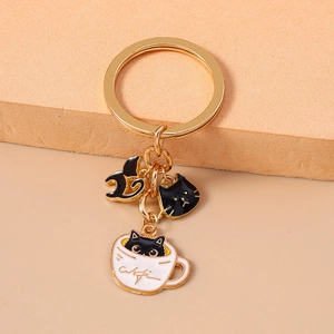 Detail of a golden keychain featuring three cute black cat charms and a white teacup pendant