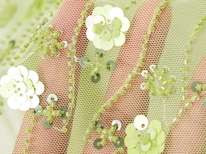 Detail view of light green mesh fabric with floral sequins and beaded embroidery detail