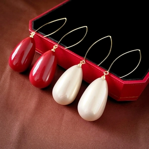 Detail of red and pearl teardrop earrings with gold hooks on a premium jewelry display box