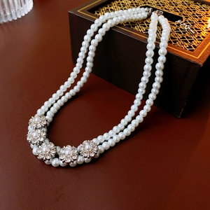 Detail of double-layer pearl necklace with rhinestone flower accents on dark wood surface