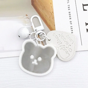 Close-up of grey bear mirror keychain with white heart leather tag and small bell