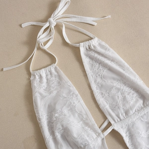 Close-up of white lace fabric detail with halter neck tie straps on a textured background