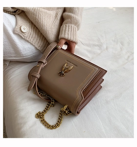 Close-up of vintage brown leather bag featuring a gold bee emblem and metal chain strap