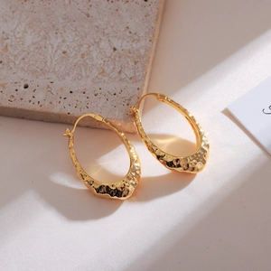 Macro detail of gold oval hoop earrings featuring a vintage hammered metal texture surface