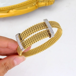 Golden mesh crossover bangle with zircon rhinestones held by a hand on white surface