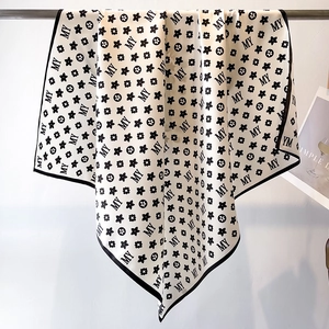 Elegant beige silk square scarf with black MY letter pattern hanging on a metal hanger