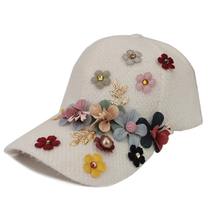 Détail de fleurs artisanales avec paillettes et perles sur une casquette blanche