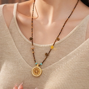 Detail of beaded tiger eye necklace with a gold hollowed floral pendant on a beige knit sweater