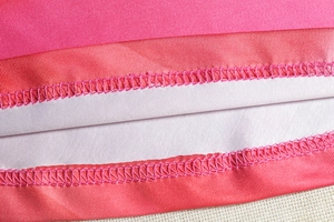 Vue macro de la couture de l'ourlet sur un haut en maille imprimé rose et orange
