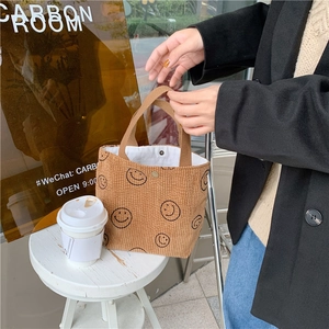 Detail of a brown corduroy handbag with a smiley face and secure metal snap closure