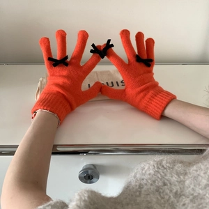 Close-up of orange knitted gloves featuring black bow details and warm texture