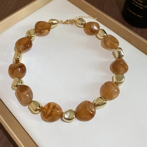 Detail view of acrylic marble beads and golden spacers on a necklace with extender chain