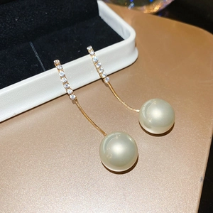 Macro detail of gold tassel earrings with zircon studs and white pearls on champagne surface