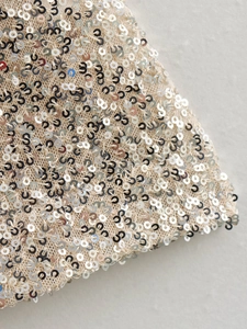 Macro shot of silver sequins on beige mesh fabric for a slim fit party dress