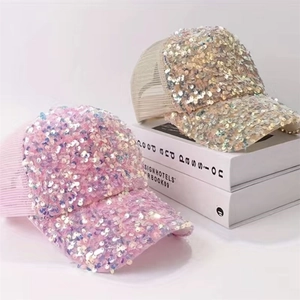 Dettaglio dei cappellini da baseball in rete con paillettes rosa e beige su libri