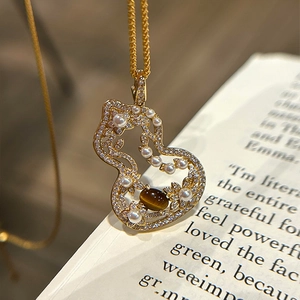 Elegant gold stainless steel gourd necklace with tiger eye stone and pearl on a book