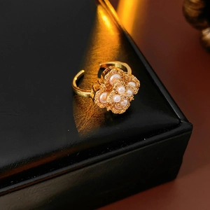 Détail d'une bague trèfle dorée avec perles posée sur un coffret en cuir noir