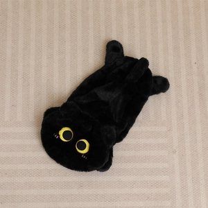 Cute black plush cat toy shell with large yellow eyes on a textured beige rug background