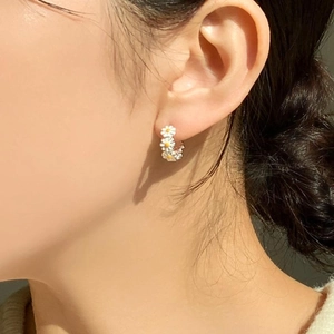 Detailed view of small white daisy hoop earrings worn on ear in natural sunlight