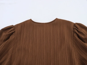Detail of round neckline and pleated shoulder on a dark brown textured smocked top