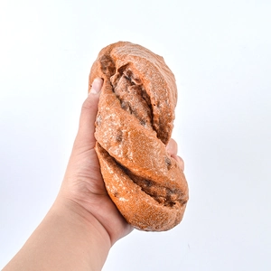Realistic artificial brown rye twisted bread model held in hand for size display