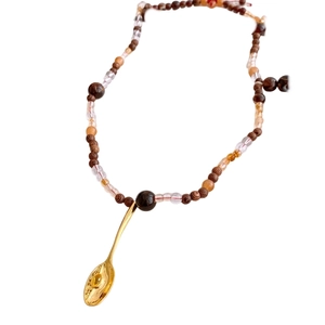 Collier rétro perles en bois et verre avec pendentif cuillère dorée sur fond blanc