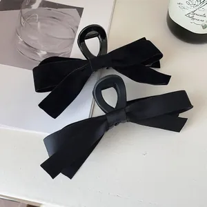 Detail showing two black bow hair clips in velvet and satin on a chic white table
