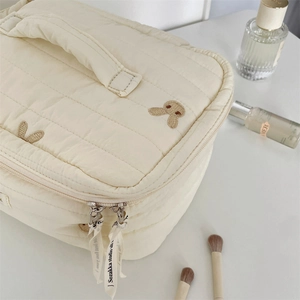 Detail of cream quilted makeup bag with cute rabbit embroidery and ribbon zipper puller