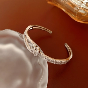 Detailed view of rose gold bow bracelet with pavé-set zircons on textured glass