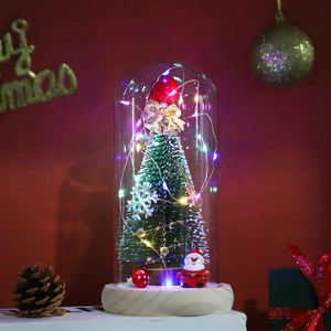 Close-up of a lit Christmas tree in a glass dome with warm LED lights and wooden base