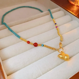 Close-up of gold plated gourd pendant necklace with colorful beads on velvet lining