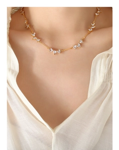 Detail of gold heart zircon necklace with sleek metal bars worn on a white shirt