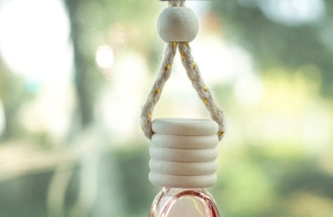 Close-up of a 6ml glass perfume bottle with a wooden cap and gold-threaded hanging cord
