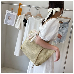 Detail of a large straw tote bag with floral ribbon and lace trim worn by a model