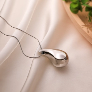 Elegant silver teardrop pendant necklace on pink silk fabric with a minimalist design