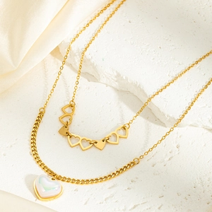 Détail d'un collier multicouche en acier doré avec pendentifs cœur sur de la soie