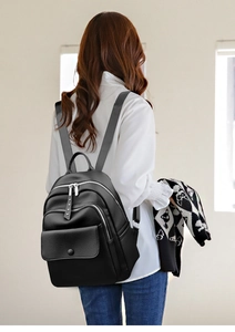 Detail view of black faux leather backpack with multiple zipper compartments and wide straps