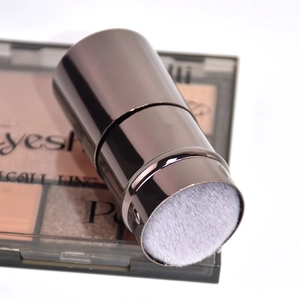 Close-up of compact makeup brush featuring dense white bristles and a polished metal handle