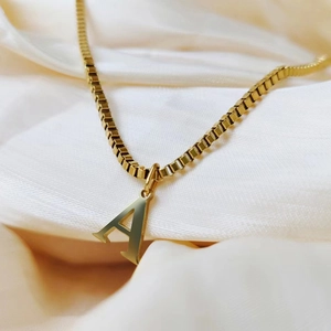 Macro detail of gold initial A pendant with polished box chain on silk background