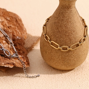 Detail of gold paperclip chain and silver anklet on ceramic vase and textured rock